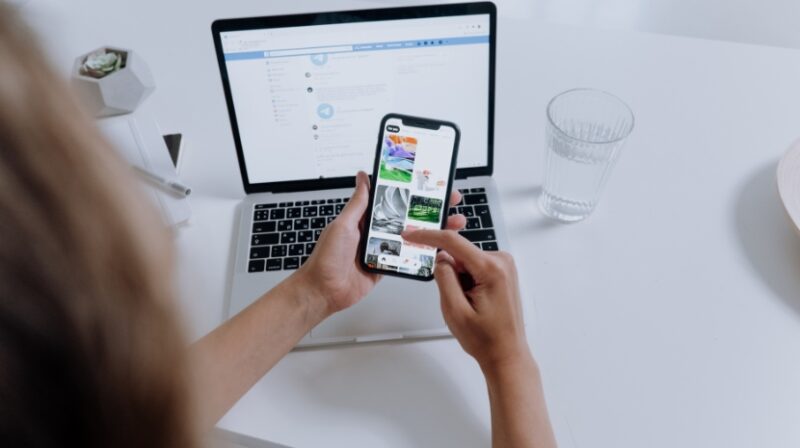 Person checking Facebook event photos on a phone with a laptop open in the background