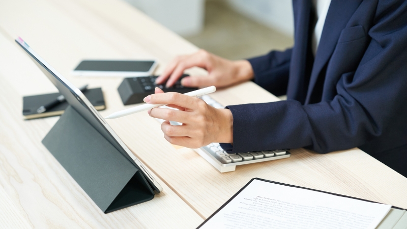 Person working on a tablet with a stylus at a desk with documents and devices